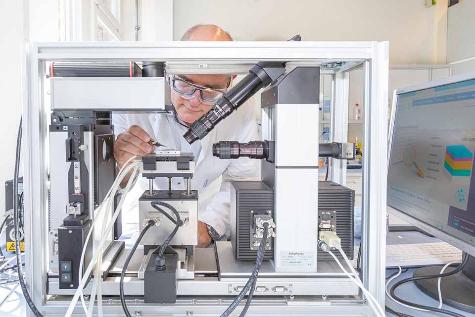 Stephan Roth bei der Probenvorbereitung der Petrowskit-Solarzelle. Ein Mann mit Schutzbrille platziert mit ruhiger Hand einen winzigen Gegenstand in einem komplexen technischen Aufbau.