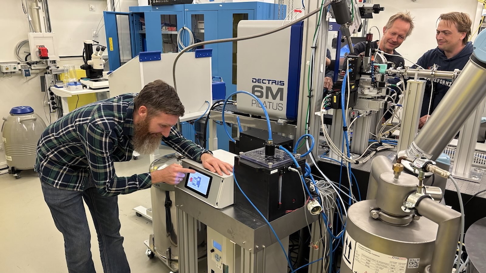 Several people are working in a modern laboratory on a complex X-ray crystallography setup. Several people are working in a modern laboratory on a complex X-ray crystallography setup.