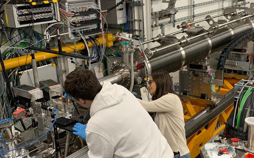 Two scientists working on complex measurement equipment with cables, sensors, and metal apparatus.
