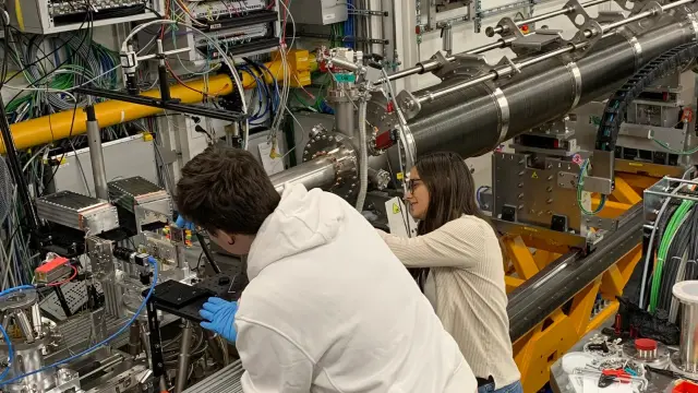 Two scientists working on complex measurement equipment with cables, sensors, and metal apparatus.