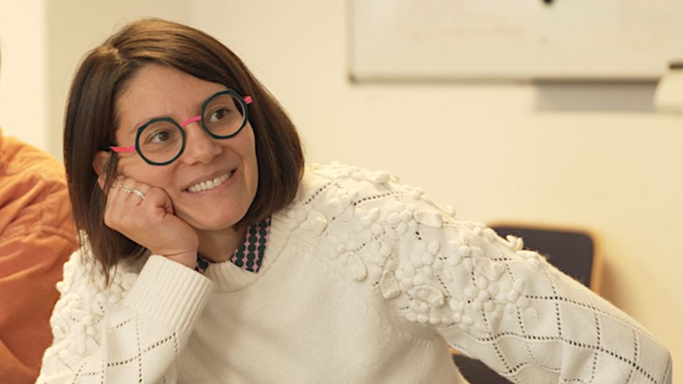 Ludovica Aperio Bella in a white sweater with round glasses, smiling indoors.