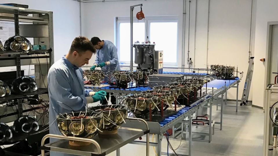 Zwei Techniker in blauer Schutzkleidung montieren Sensormodule für das IceCube-Upgrade in einem Reinraum.