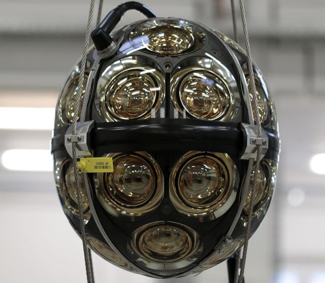Spherical module with multiple lenses for the IceCube upgrade, suspended by cables in a lab setting.