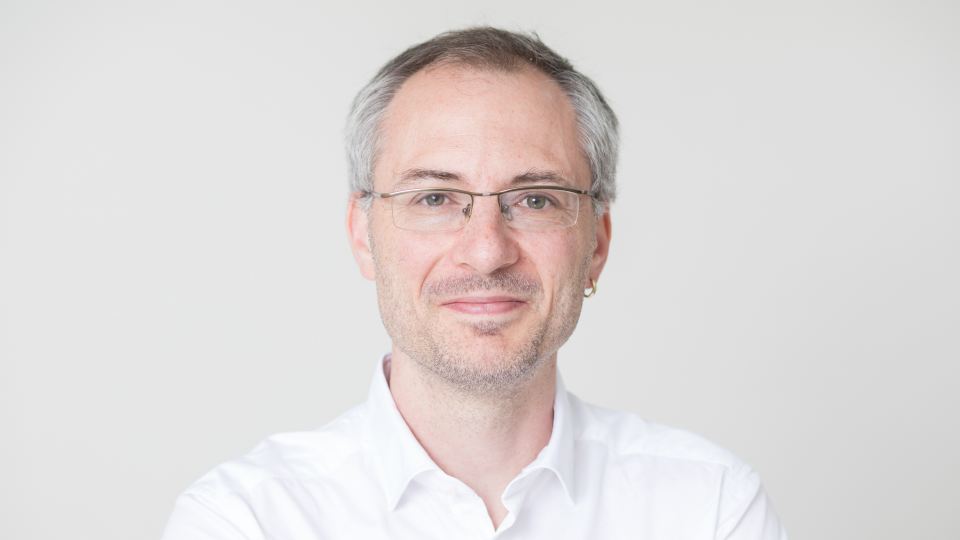 Portrait von Prof. Dr. Philipp Neumann in weißem Hemd vor neutralem Hintergrund.