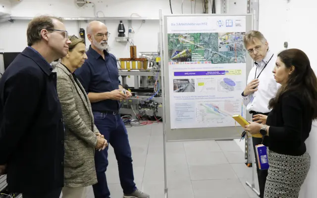 Five people standing in a laboratory discussing the work areas of PITZ in front of a poster.