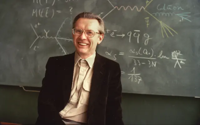Herwig Schopper bei einem Portrait vor einer Tafel mit physikalischen Formeln und Diagrammen, trägt Sakko und Hemd.