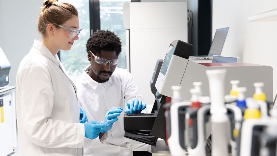Wissenschaftler:innen arbeiten mit Schutzbrillen und Labortechnik in einem modernen Forschungslabor.