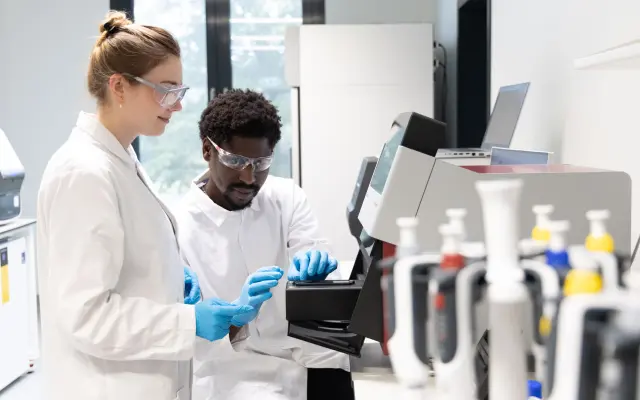 Scientists wearing safety goggles work with laboratory equipment in a modern research lab.
