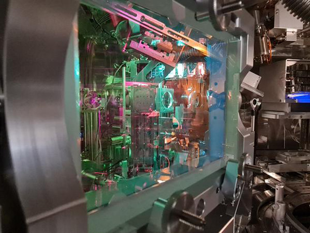 Komplexer Aufbau eines Experiments. Zu sehen sind präzise optische und mechanische Komponenten, farbig beleuchtete Apparaturen sowie hochmoderne Messtechnik.