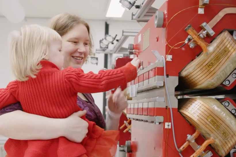 In der Testwerkstatt hält Ingenieurin Jana Barker ihre Tochter auf dem Arm. Gemeinsam betrachten sie zur Vermessung aufgebaute Magnete. In der Testwerkstatt hält Ingenieurin Jana Barker ihre Tochter auf dem Arm. Gemeinsam betrachten sie zur Vermessung aufgebaute Magnete.